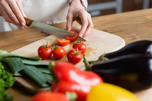 Teilansicht einer jungen erwachsenen Frau, die in der modernen Küche Kirschtomaten auf dem Schneidebrett schneidet — Stockfoto