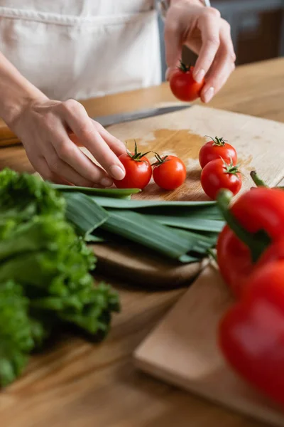 Visão parcial das mãos femininas segurando tomates cereja na tábua de corte na cozinha moderna — Fotografia de Stock