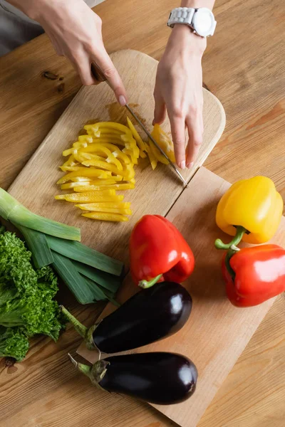 Vista superior de mãos femininas picando pimentão amarelo na tábua de corte na mesa na cozinha — Fotografia de Stock