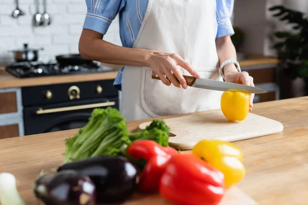 Vista parziale della giovane donna adulta che taglia il pepe giallo sul tagliere in cucina — Foto stock