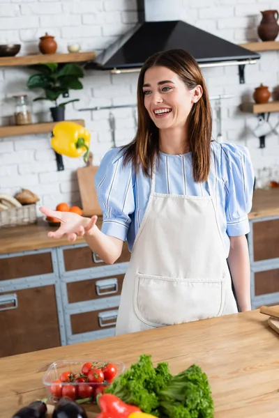 Усміхнена молода доросла жінка кидає жовтий перець в повітря на кухні — стокове фото