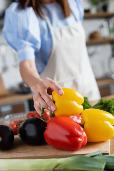 Vue partielle de jeune femme adulte touchant le poivron jaune dans la cuisine — Photo de stock