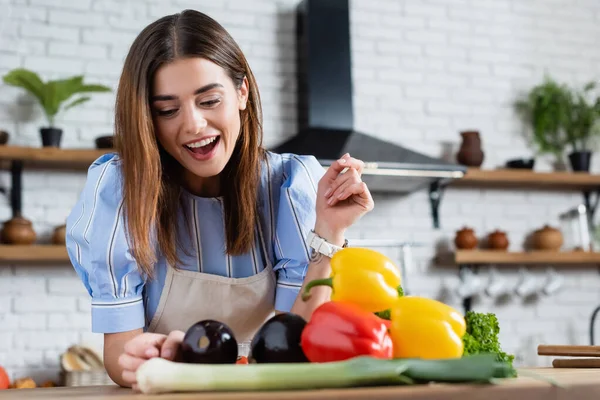 Positivo jovem mulher adulta olhando para legumes frescos na mesa na cozinha — Fotografia de Stock