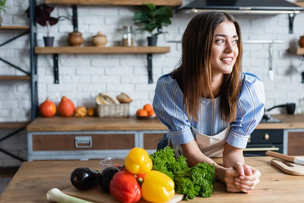 Sorridente giovane donna adulta in piedi vicino al tavolo con verdure in cucina — Foto stock