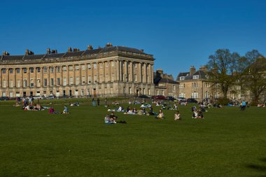 Bath, Birleşik Krallık - 25 Nisan 2021: Royal Crescent in Bath, Somerset, İngiltere. İnsanlar çimenlerde oturur güneşli bir bahar gününün tadını çıkarırlar..