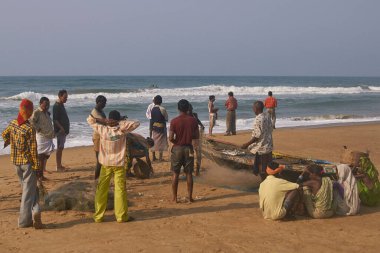 Puri, Odisha, Hindistan - 14 Mayıs 2008: Balıkçılar balık ağlarından balıkları toplarken kadınlar yerde oturup balıkları pazara götürmek için bekliyorlar.