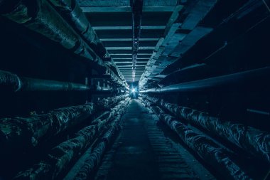 Karanlık yeraltı beton iletişim tüneli soğuk renklerde borular ve kablolarla.