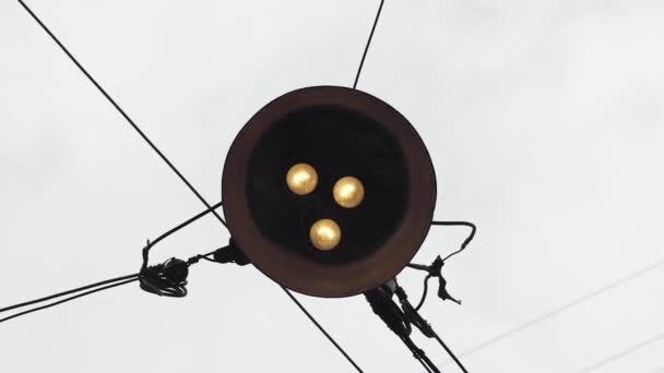 Ancien réverbère vintage avec trois lampes en tungstène est suspendu sur des câbles sur un fond de ciel gris. Vue de bas en haut. — Video