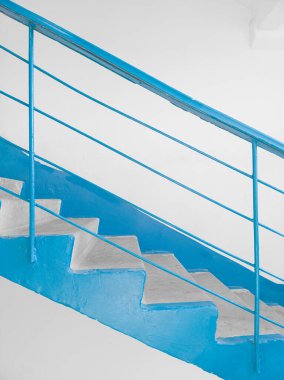 Arkadaki beyaz duvara maviyle boyanmış merdivenlerin yan görüntüsü. Sovyet yerleşim yerindeki tipik merdivenler..