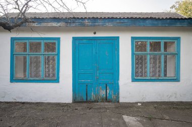 Ormanda mavi kapıları ve pencereleri olan eski, eski püskü, bir katlı, beyaz tuğlalı bir ev..
