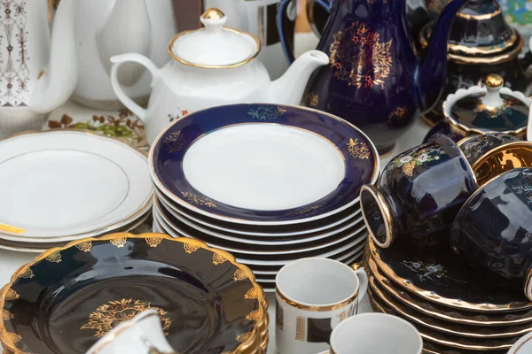 Antika pazarında koyu mavi ve altın kenarlı porselen tabaklar ve çay setleri yığılmış. Kyiv, Ukrayna, 5 Ekim 2025.