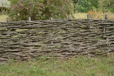 Ot ve çim ön planda birbirine dolanmış dallardan yapılmış ahşap ahşap çitler..