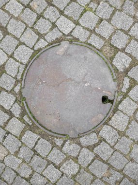 Yeşil yosunlu kaldırım taşı döşenmiş eski yuvarlak metal rögar kapağı..