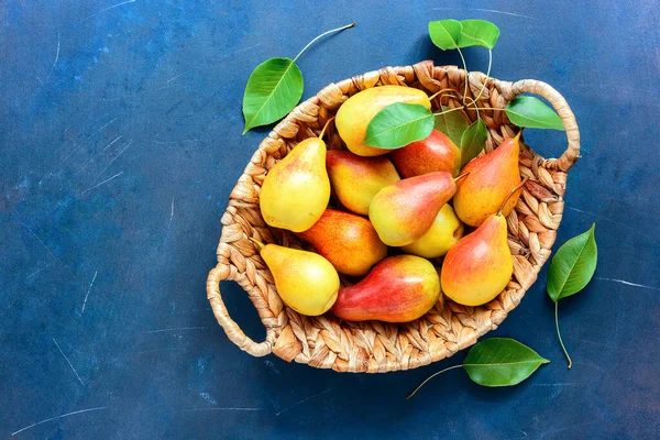 Fresh pears with leaves in a basket. Red-yellow pears. Blue rustic background. Top view