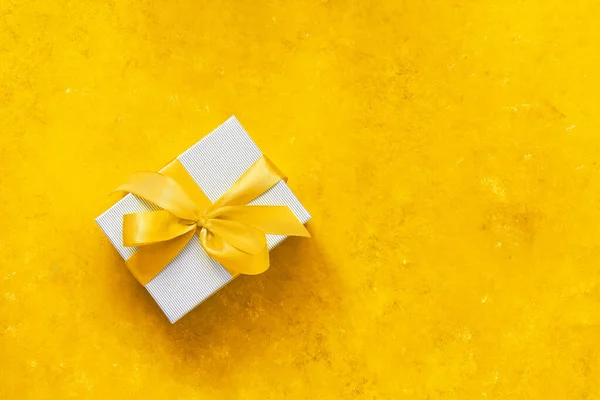Gray box with yellow ribbon on yellow grunge background. The trendy color of 2021 is yellow and gray. Holiday concept. Top view, flat lay