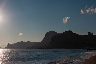 Denizde bulutsuz bir gökyüzüne karşı dağlar