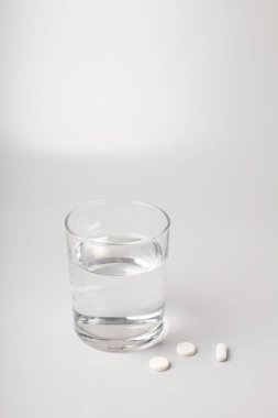 Bir bardak su ve beyaz arka planda haplar.