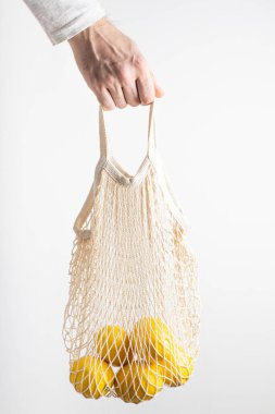 Bir adamın eli olgun limonlarla dolu çevre dostu bir çanta tutuyor.