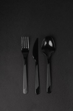 Siyah arka planda plastik tek kullanımlık bıçak, kaşık ve çatal.