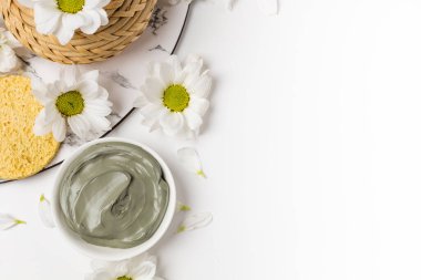 Beyaz arka planda çiçeklerle kuru ve ıslak doğal kil maskesi.