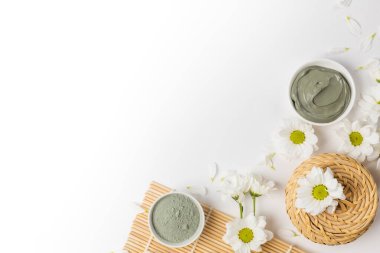 Beyaz arka planda çiçeklerle kuru ve ıslak doğal kil maskesi.