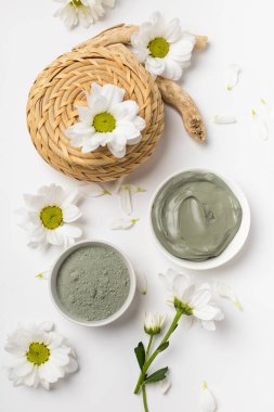 Beyaz arka planda çiçeklerle kuru ve ıslak doğal kil maskesi.