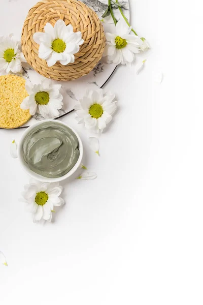 Beyaz arka planda çiçeklerle kuru ve ıslak doğal kil maskesi.