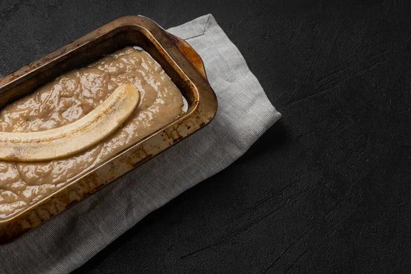 Raw banana bread dough in rectangular baking dish on black background