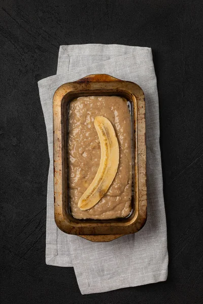 Raw banana bread dough in rectangular baking dish on black background