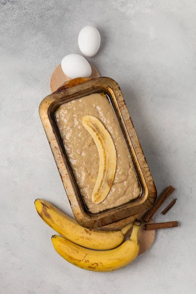 Raw banana bread dough in rectangular shape with ingredients on light background