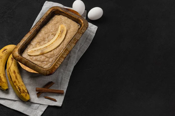 Raw banana bread dough in rectangular baking dish with ingredients on black background