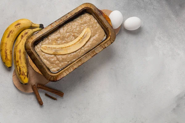 Raw banana bread dough in rectangular shape with ingredients on light background