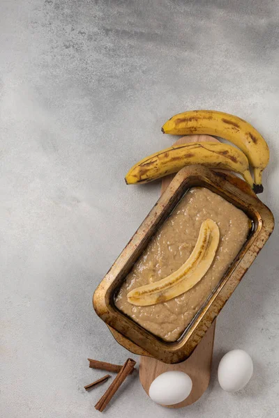 Raw banana bread dough in rectangular shape with ingredients on light background
