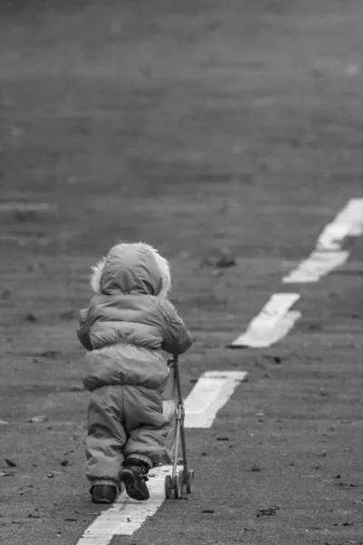 The child is walking along the road. Kid back view. Go your own way. Unidentified girl with a stroller. The road to life. Small man. Children\'s independence. Winter coveralls. Intended goal.