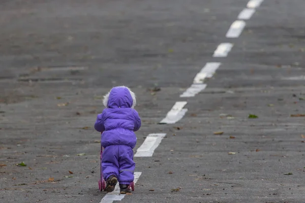 The child is walking along the road. Kid back view. Go your own way. Unidentified girl with a stroller. The road to life. Small man. Children\'s independence. Winter coveralls. Intended goal.