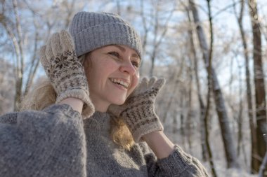 Gri şapkalı ve kazaklı mutlu bir kız. Geyik desenli örülmüş bir kazak. Eldivenler sıcak olsun. Orijinal Ukrayna el yapımı giysileri. Şenlik havası. 40 yaş üstü güzel bir kadın. Buz gibi temiz hava. Kış doğası. Karla serp.