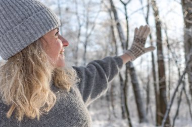 Gri şapkalı ve kazaklı mutlu bir kız. Geyik desenli örülmüş bir kazak. Eldivenler sıcak olsun. Orijinal Ukrayna el yapımı giysileri. Şenlik havası. 40 yaş üstü güzel bir kadın. Buz gibi temiz hava. Kış doğası. Karla serp.