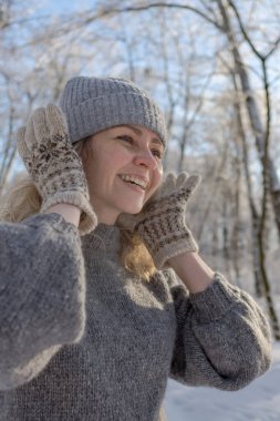 Gri şapkalı ve kazaklı mutlu bir kız. Geyik desenli örülmüş bir kazak. Eldivenler sıcak olsun. Orijinal Ukrayna el yapımı giysileri. Şenlik havası. 40 yaş üstü güzel bir kadın. Buz gibi temiz hava. Kış doğası. Karla serp.