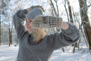 Gri şapkalı ve kazaklı mutlu bir kız. Geyik desenli örülmüş bir kazak. Eldivenler sıcak olsun. Orijinal Ukrayna el yapımı giysileri. Şenlik havası. 40 yaş üstü güzel bir kadın. Buz gibi temiz hava. Kış doğası. Karla serp.