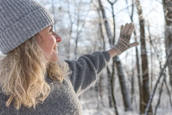 Gri şapkalı ve kazaklı mutlu bir kız. Geyik desenli örülmüş bir kazak. Eldivenler sıcak olsun. Orijinal Ukrayna el yapımı giysileri. Şenlik havası. 40 yaş üstü güzel bir kadın. Buz gibi temiz hava. Kış doğası. Karla serp.