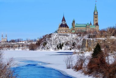 Parlamento binaları ve çoğunlukla donmuş Ottawa Nehri manzarası.