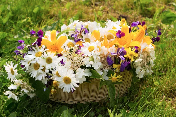 Una cesta llena de flores de campo sobre una hierba verde — Foto de Stock