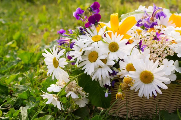 Un panier plein de fleurs de champ sur une herbe verte — Photo