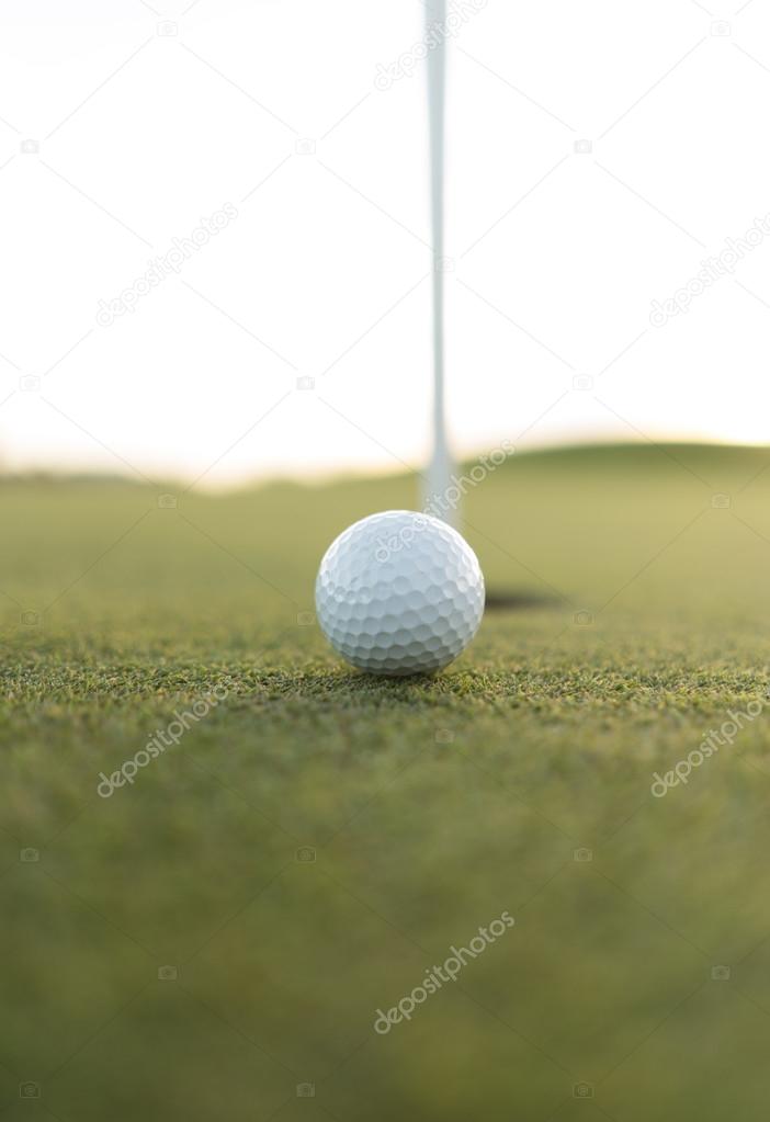 Gold ball close to cup hole on putting green