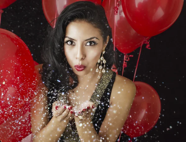 Piękna młoda kobieta dmuchanie konfetti - tło czerwone balony — Zdjęcie stockowe