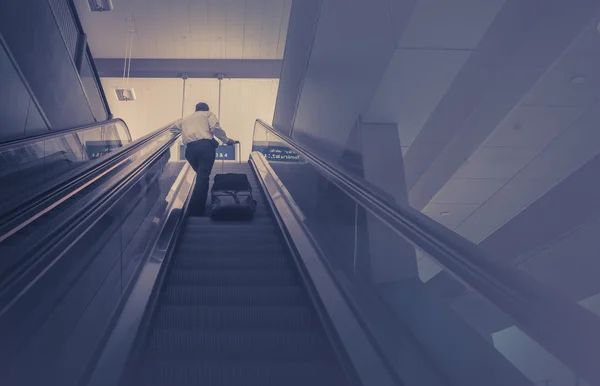 Biznes człowiek biorąc bagażu schodami ruchomymi na najwyższym piętrze. Obrazek koncepcyjny podróży biznesowych — Zdjęcie stockowe