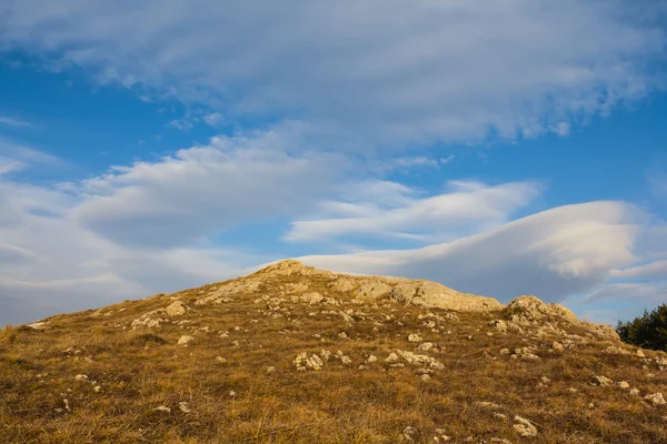 Chão colina em um fundo azul nuvens — Fotografia de Stock