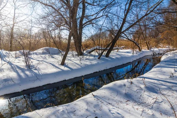 Небольшая река течет через зимний снежный лес — стоковое фото