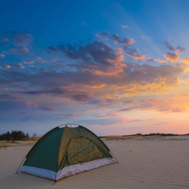 small touristic tent in a sandy desert under dramatic evening cloudy sky, natural travel background