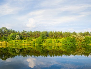 Sakin bir yaz nehri, ormanlık bir sahil bulutlu bir gökyüzü altında, yaz kırsal kesim doğal arka plan
